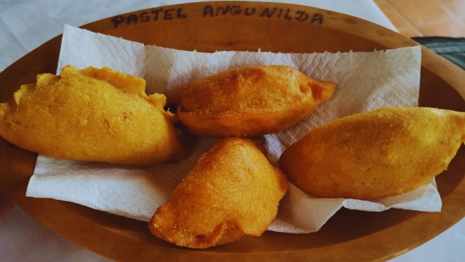 A imagem mostra quatro pastéis de angu em uma bandeia de madeira