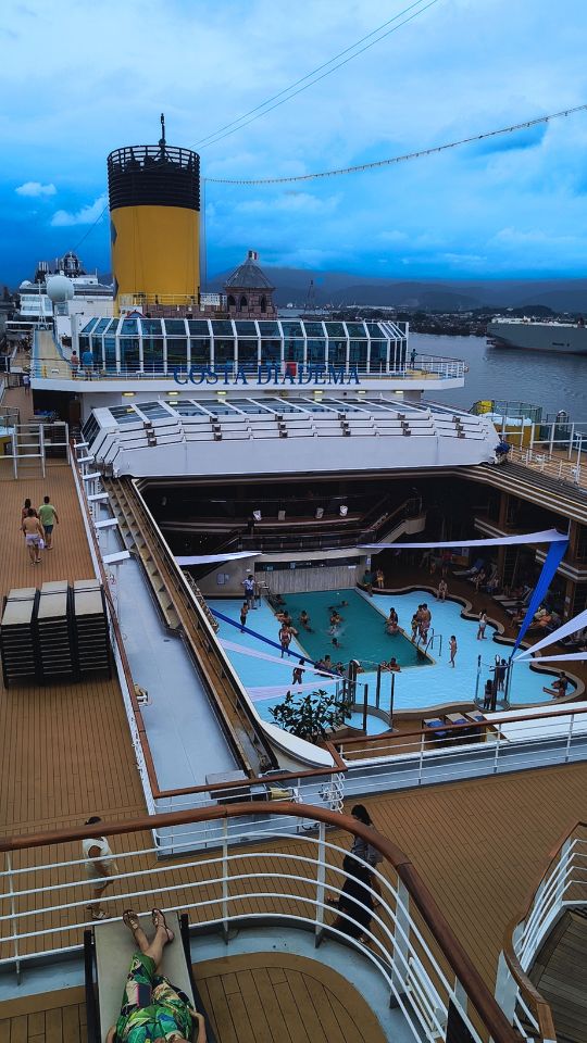 Vista da área da piscina na Ponte 12 do navio Costa Diadema, com passageiros relaxando.