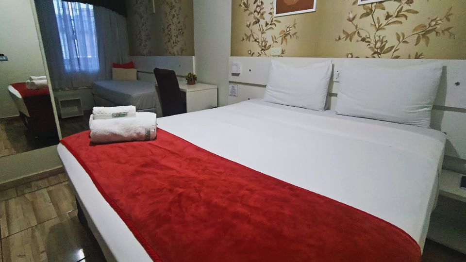 Quarto com uma cama de casal e uma cama de solteiro, mesinha de escritório, frigobar e televisão de tela plana