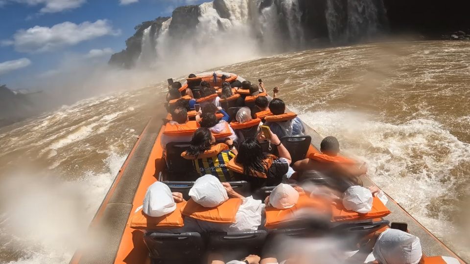 O barco acelera diretamente em direção ao Salto Três Mosqueteiros, a água começa a cair cada vez mais forte sobre os passageiros