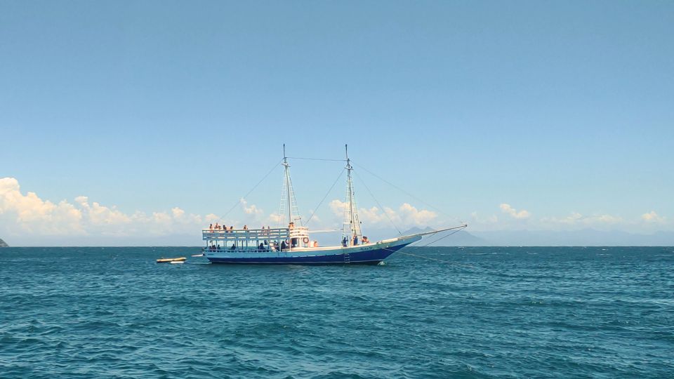 Uma escuna com turistas navega pelo mar azul de Búzios, com formações rochosas ao fundo